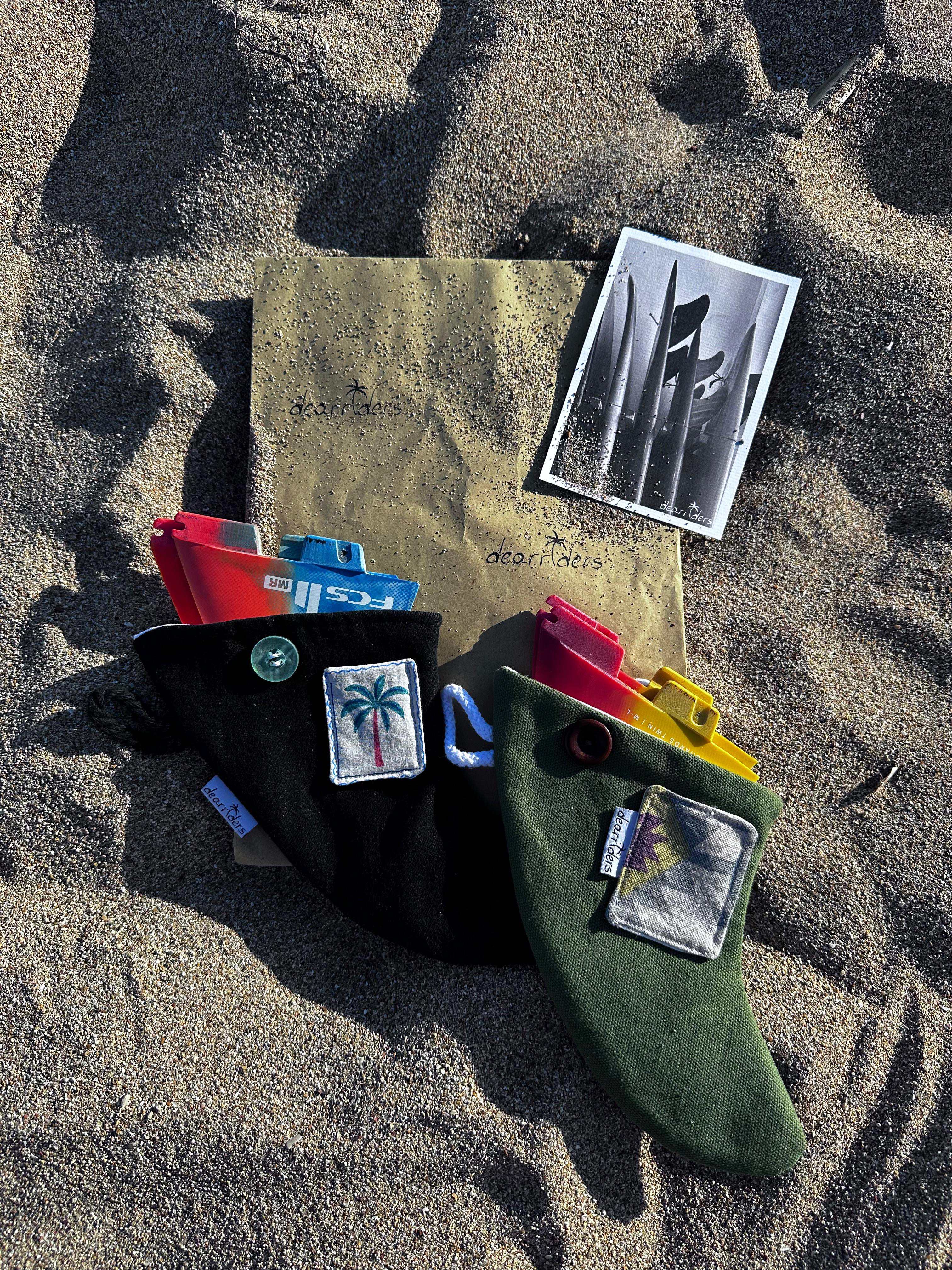 Two dearriders surf fin cases holding colorful fins on beach sand