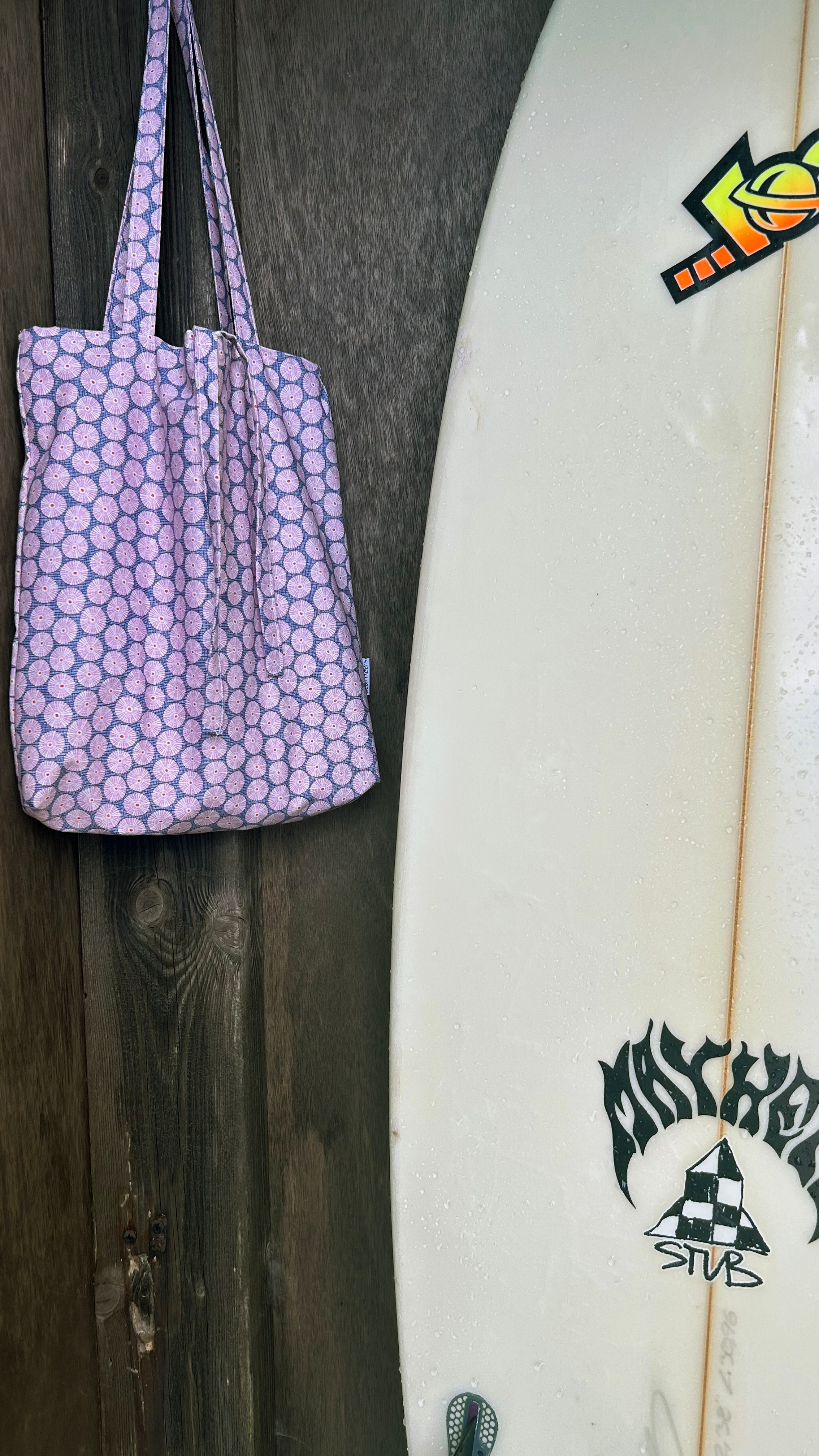 Lavender sea-urchin patterned handmade tote bag hanging next to a surfboard